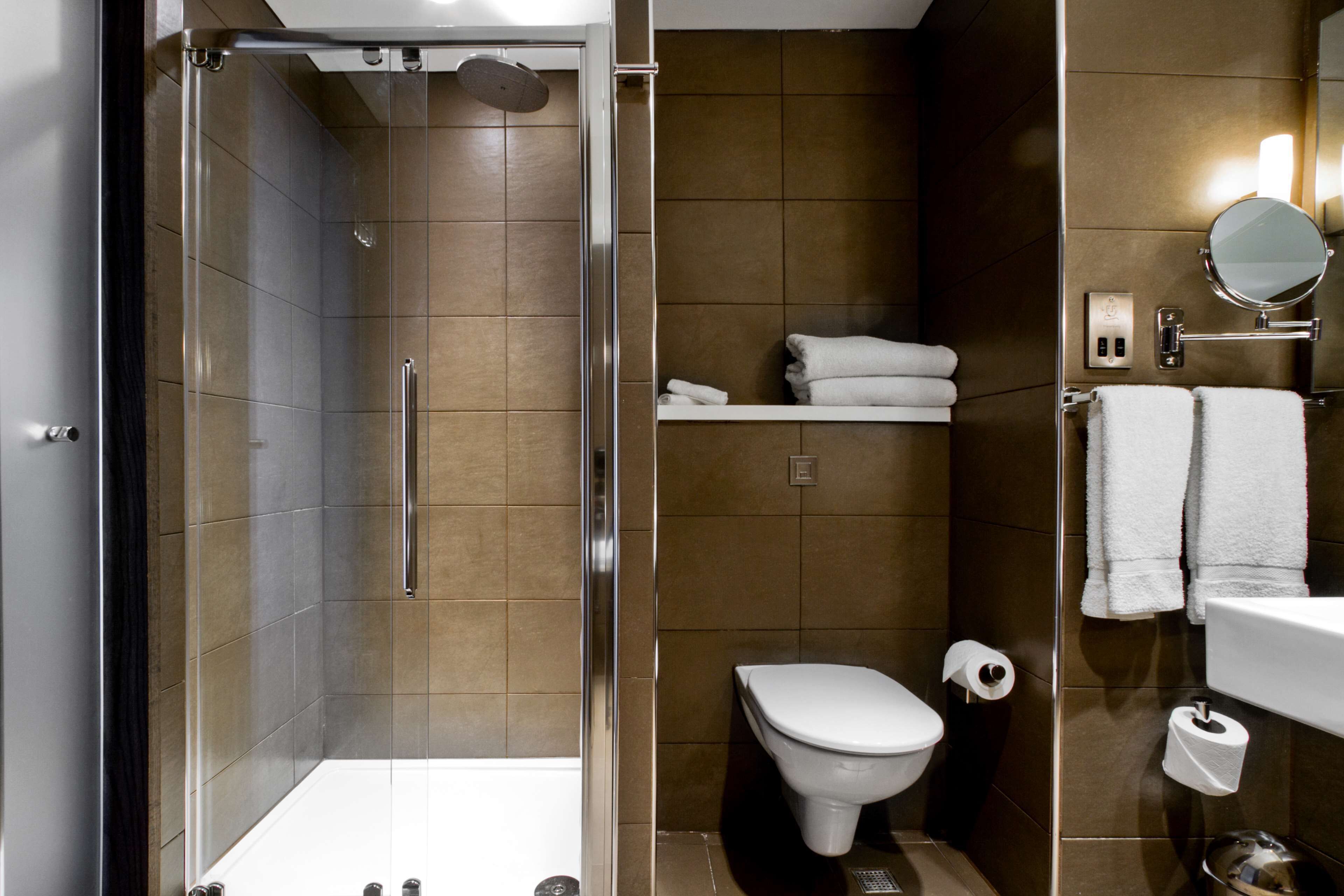 A modern bathroom with a glass-enclosed shower, a toilet, and a sink with a mirror.
