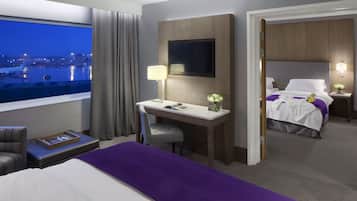 A hotel room with a desk, a bed, a TV, and a view of the airport.