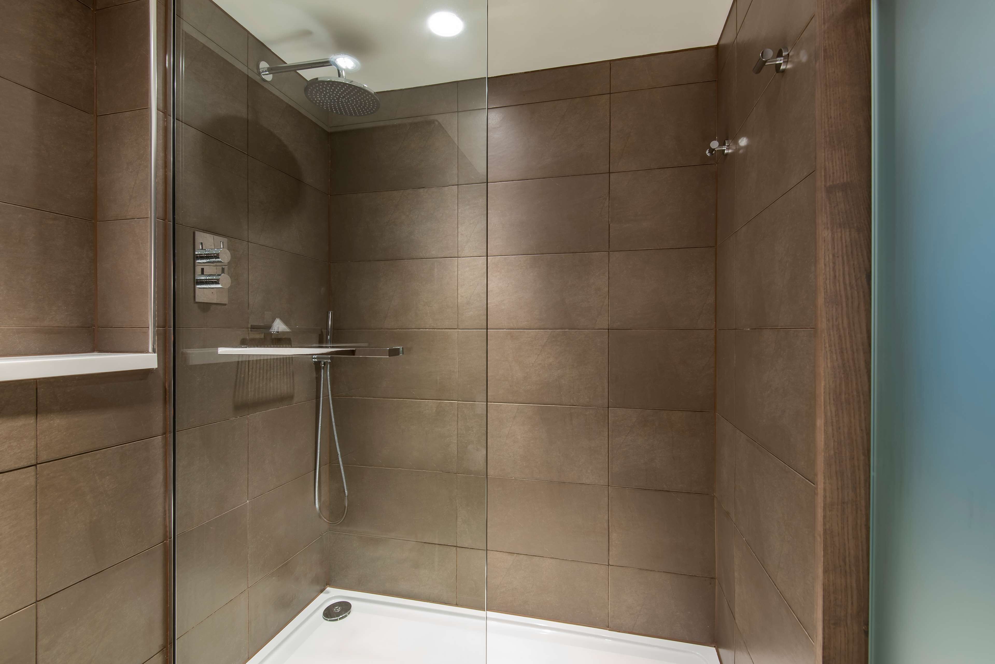 A modern shower with a glass door, a handheld showerhead, and a wall-mounted towel rack.