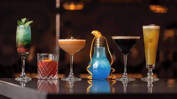Eine Bar mit verschiedenen Getränken, darunter ein Cocktail mit Minze, ein blaues Getränk in einer Vase und ein hohes Glas mit einem gelben Getränk.