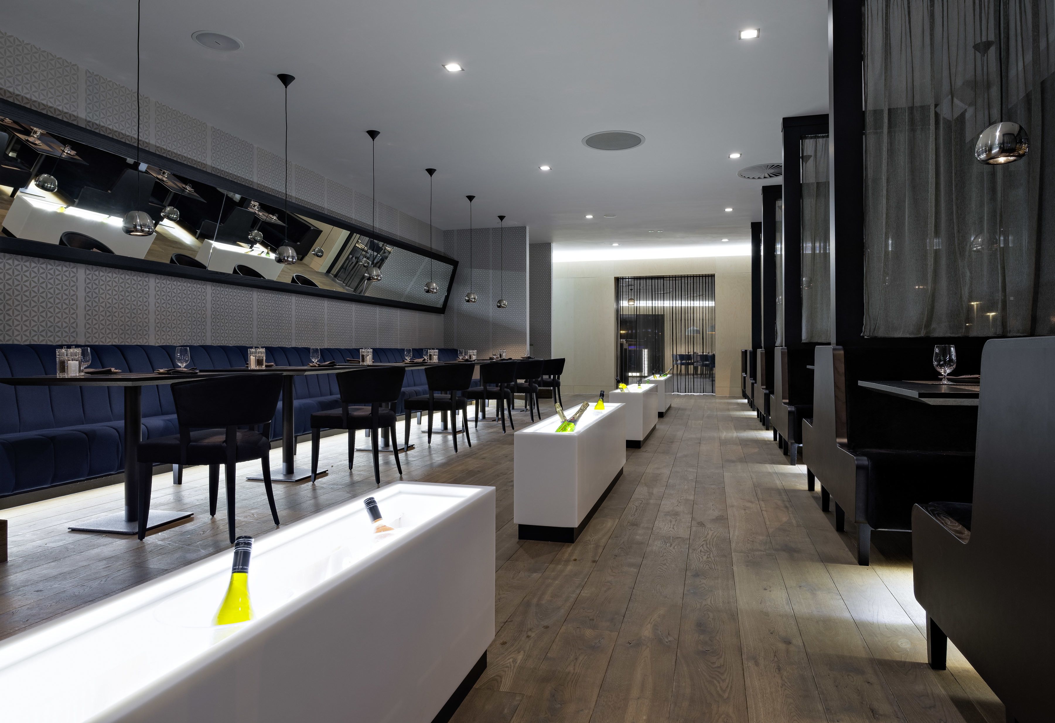 Ein modernes Restaurant mit einer langen Theke, schwarzen Stühlen und einer Spiegelwand.