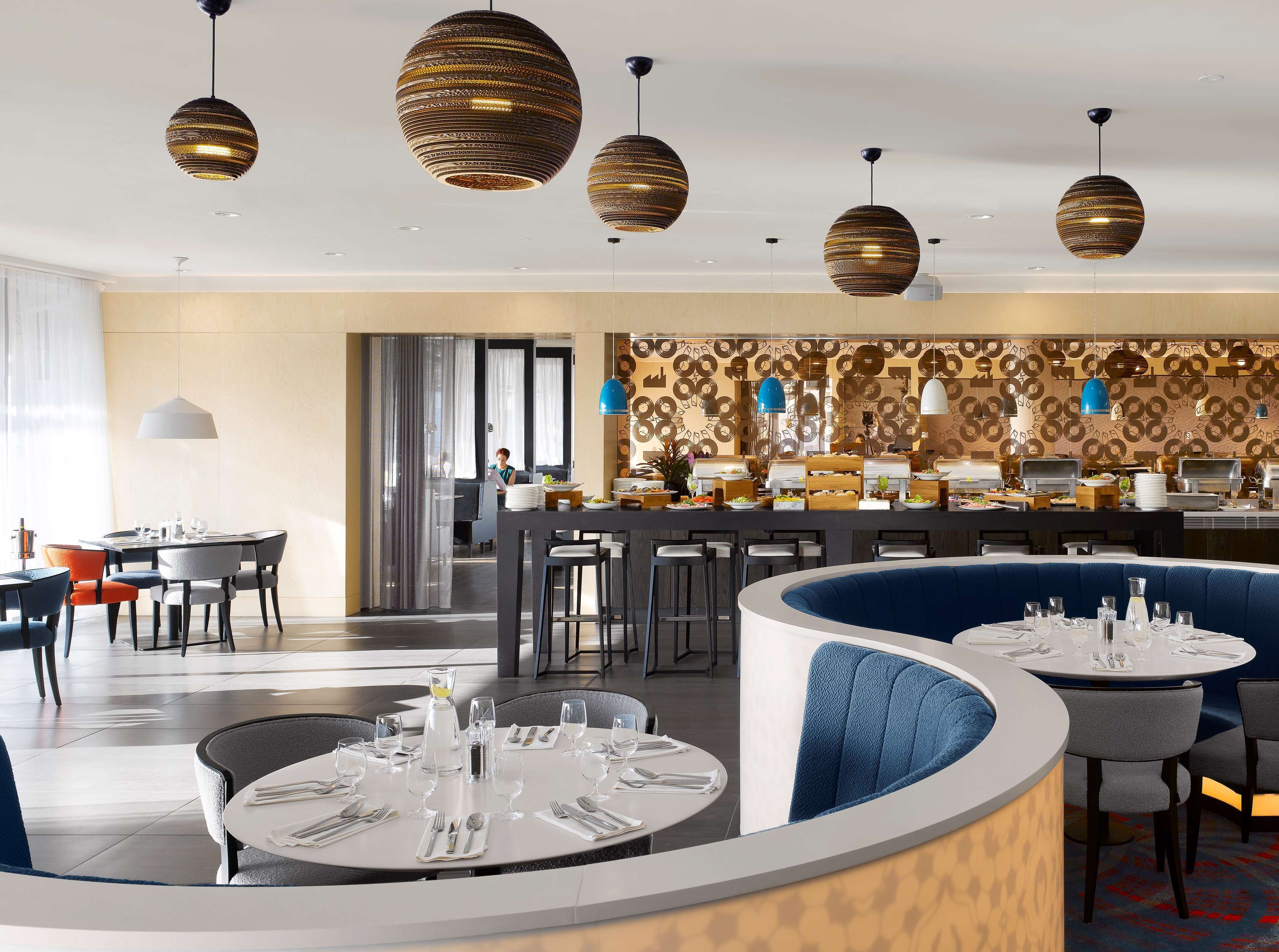 A modern restaurant with round tables, blue booths, and patterned wall decor.