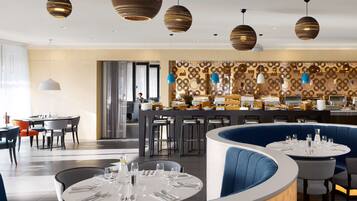 A modern restaurant with round tables, blue booths, and patterned wall decor.