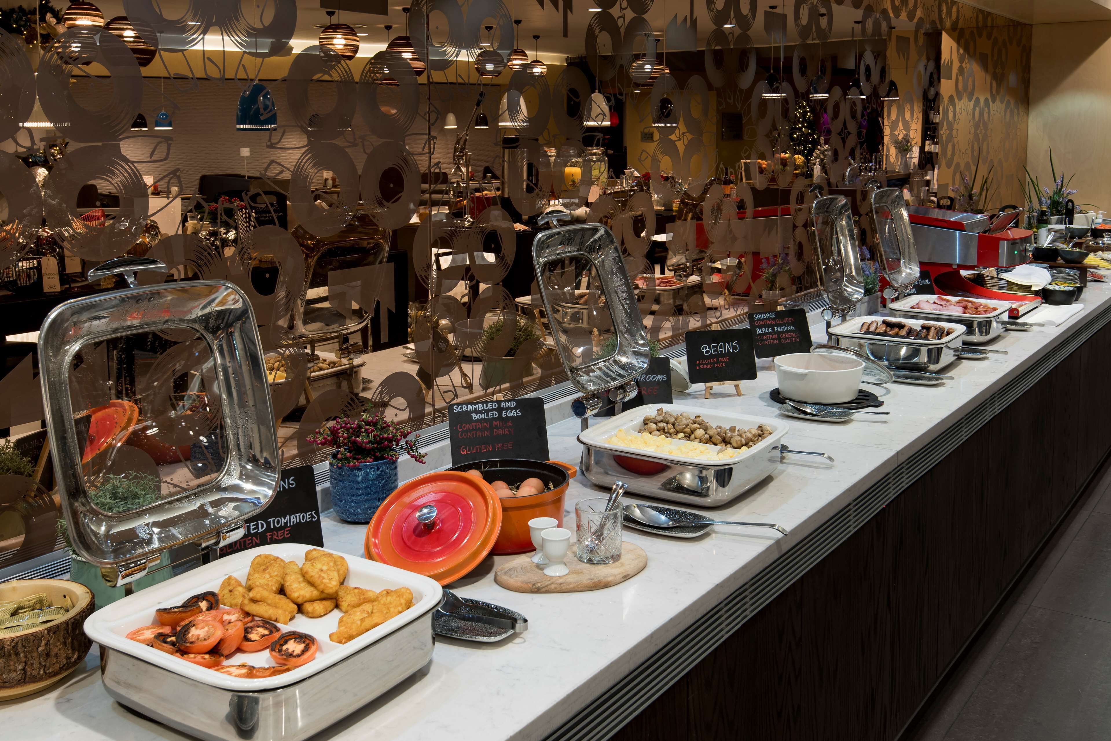 A buffet with various food items and utensils, including scrambled eggs, tomatoes, and bowls.