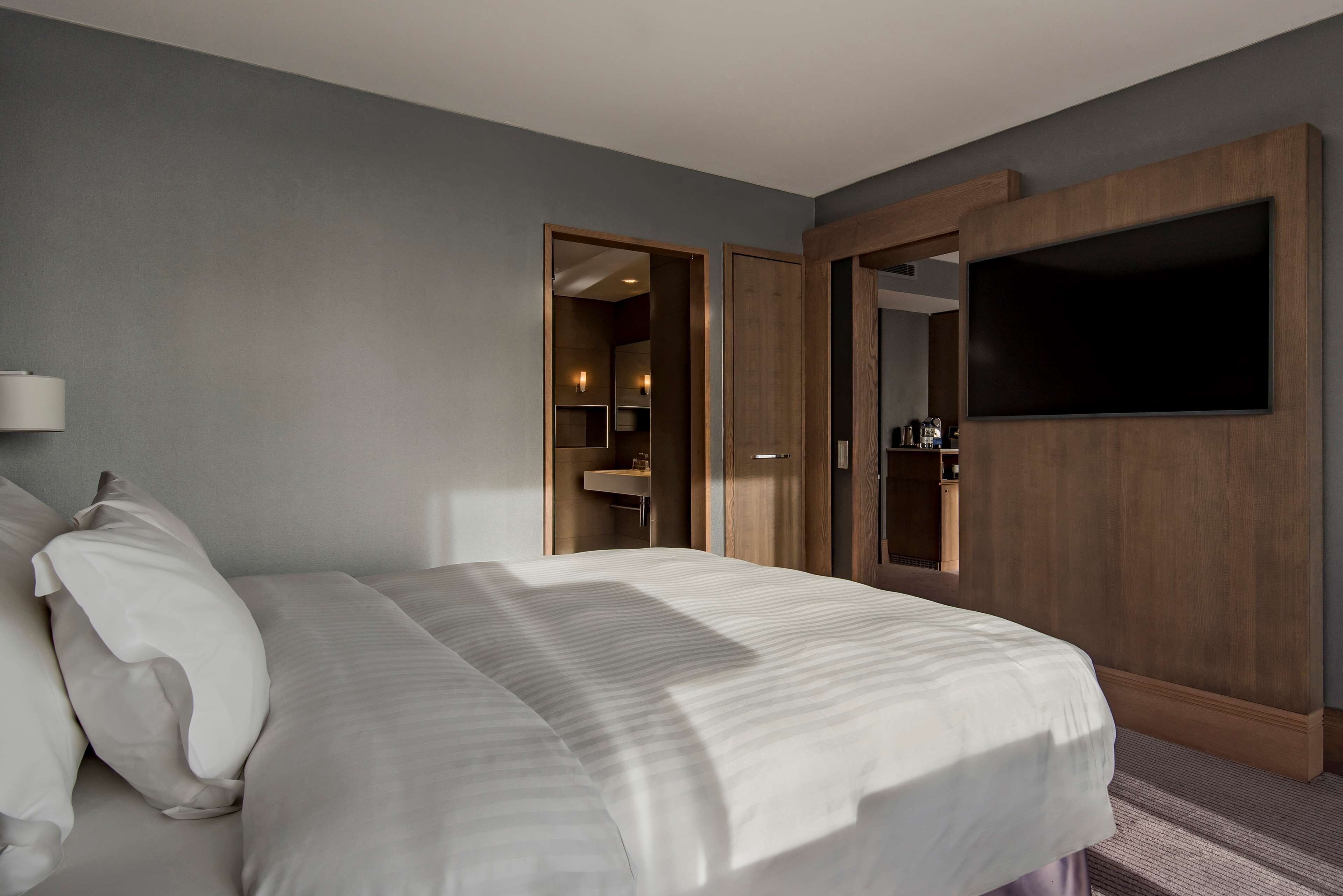 A hotel room with a large bed, a wooden wardrobe, and a television mounted on the wall.