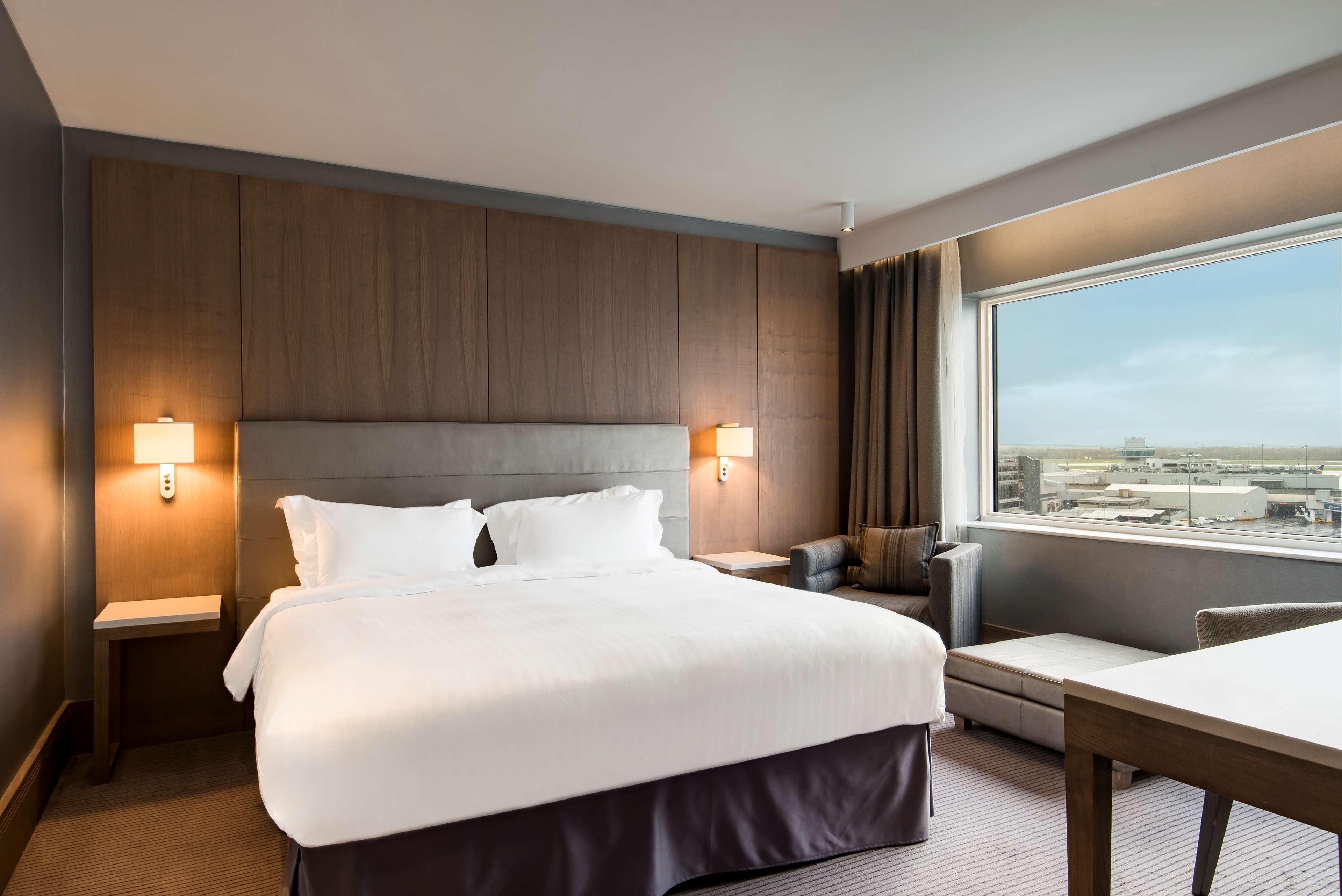 Habitación de hotel con una cama grande, lámparas de noche, un escritorio y vistas a la ciudad por la ventana.