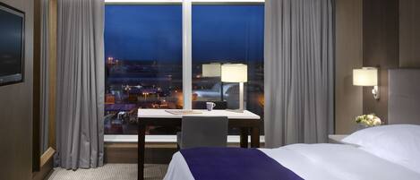 A hotel room with a bed, a desk, a chair, a TV, and a window with curtains.