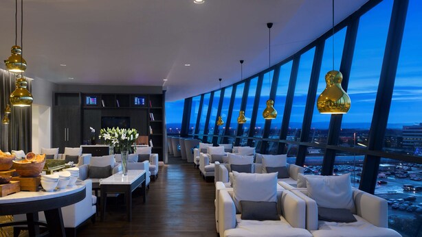 A modern lounge with a city view, featuring sofas, tables, and pendant lighting.