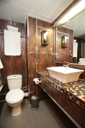 A modern bathroom with a glass-enclosed shower, a white toilet, a sink with a tiled countertop, and a mirror above the sink. - The Bruce Hotel (Glasgow)