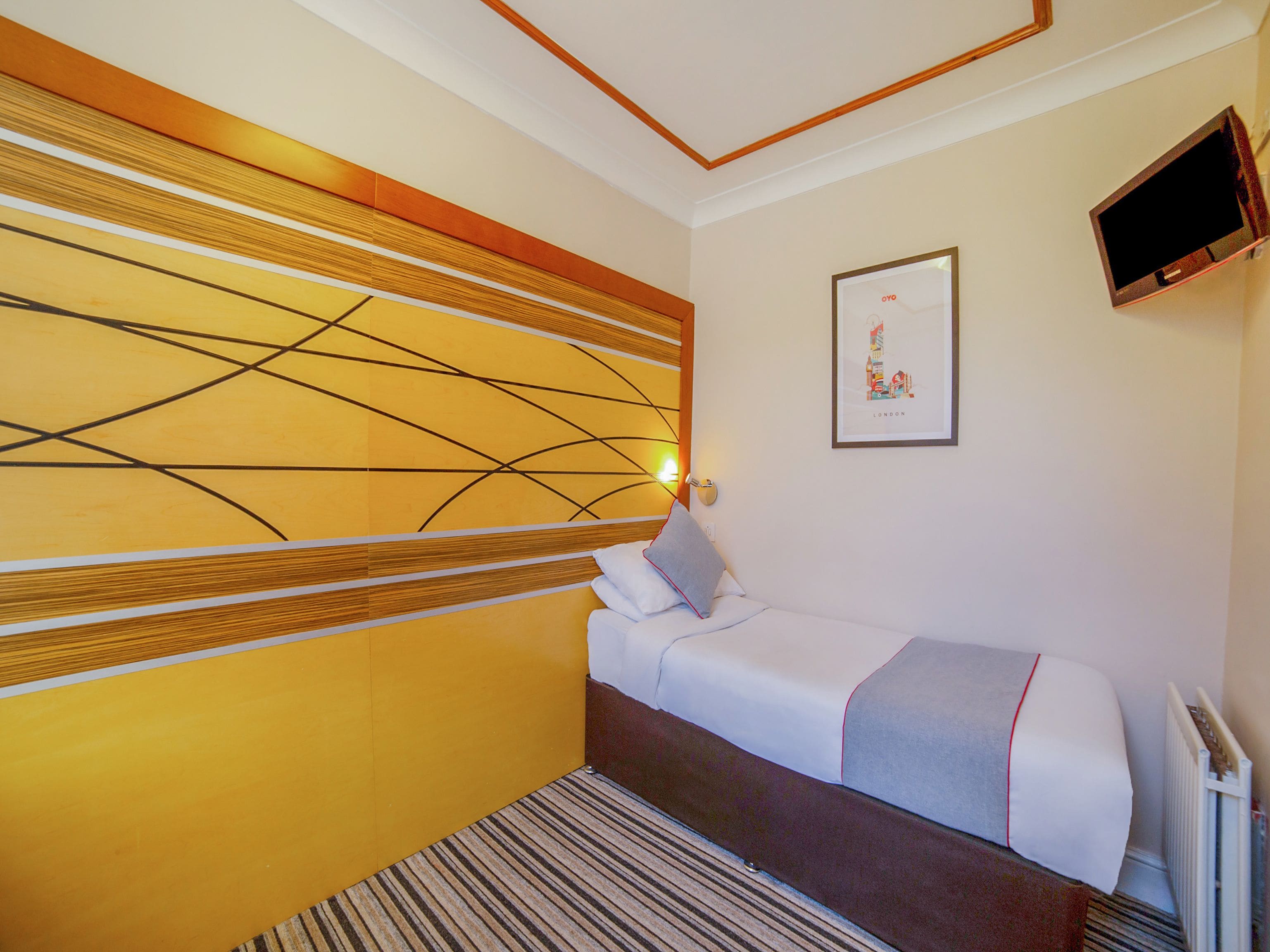 A hotel room with a bed, a wall-mounted TV, and a framed picture.