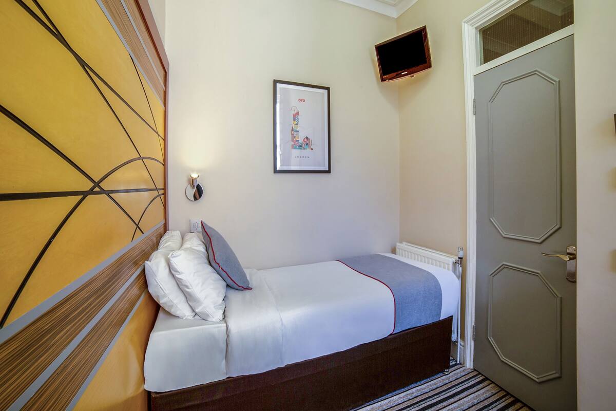 A neatly made bed with a gray and white duvet, a framed picture on the wall, and a television mounted on the wall.