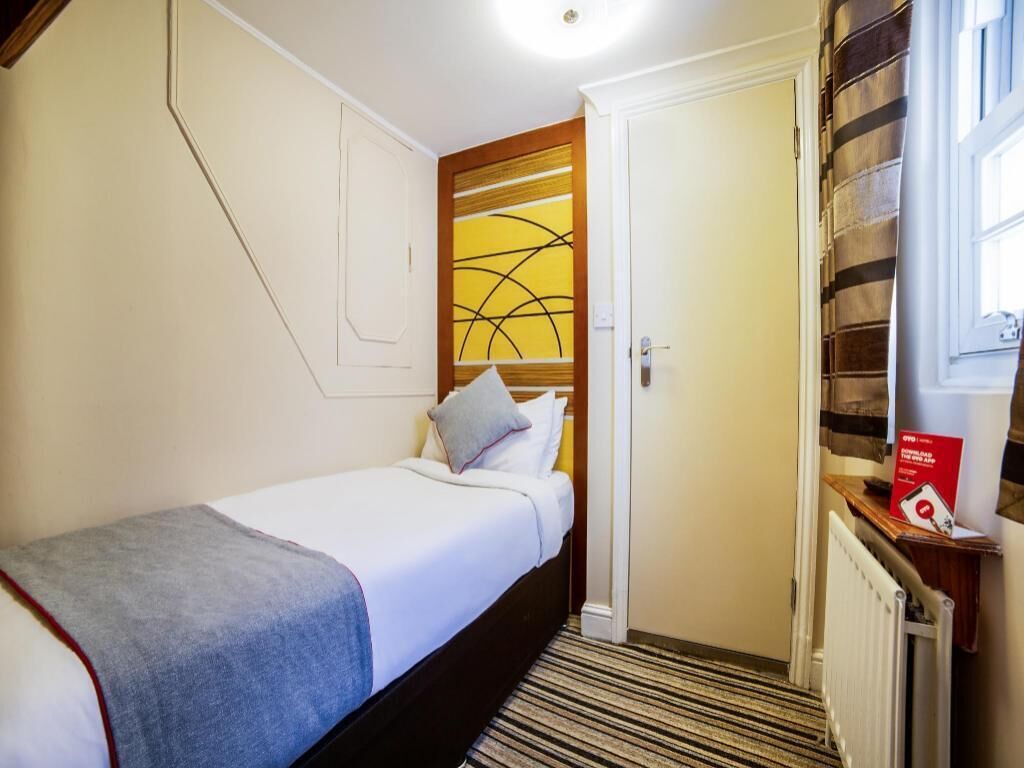 A hotel room with a bed, a door, a radiator, and a window.