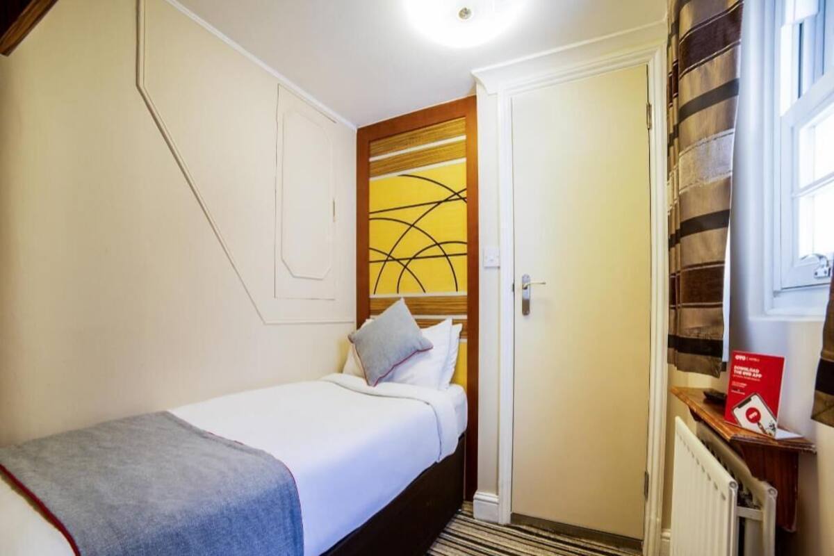 A hotel room with a bed, a door, a radiator, and a window.