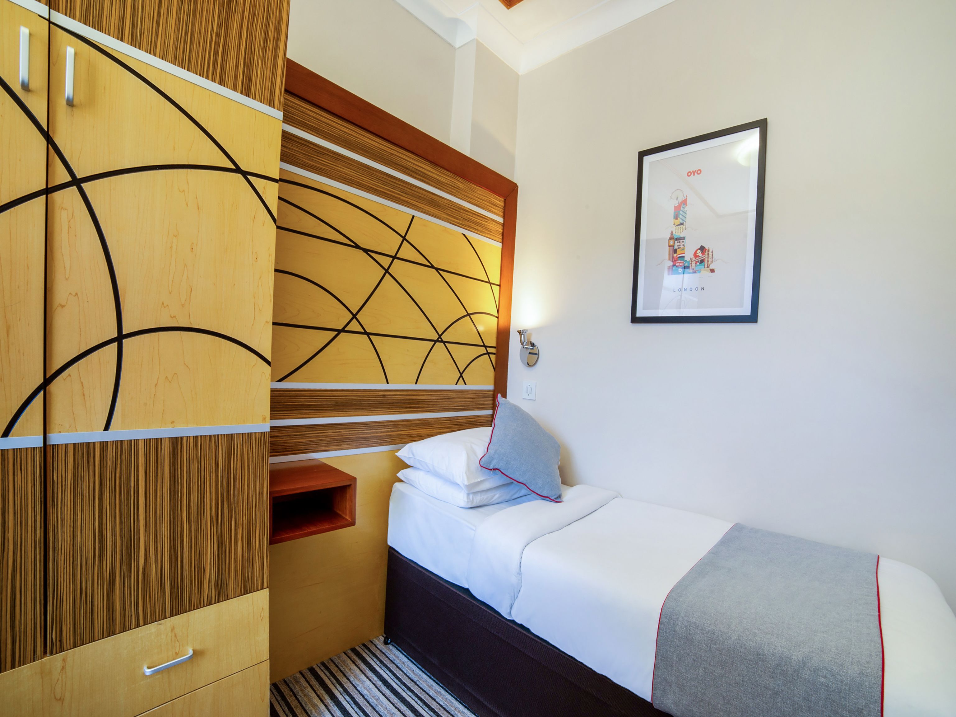 Une chambre d’hôtel avec un lit, une armoire en bois, une étagère fixée au mur et un tableau encadré.