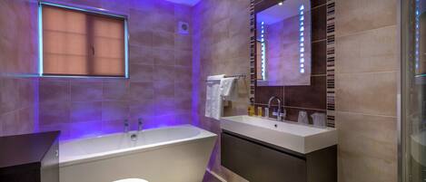 A modern bathroom with a bathtub, toilet, vanity, and a large mirror.