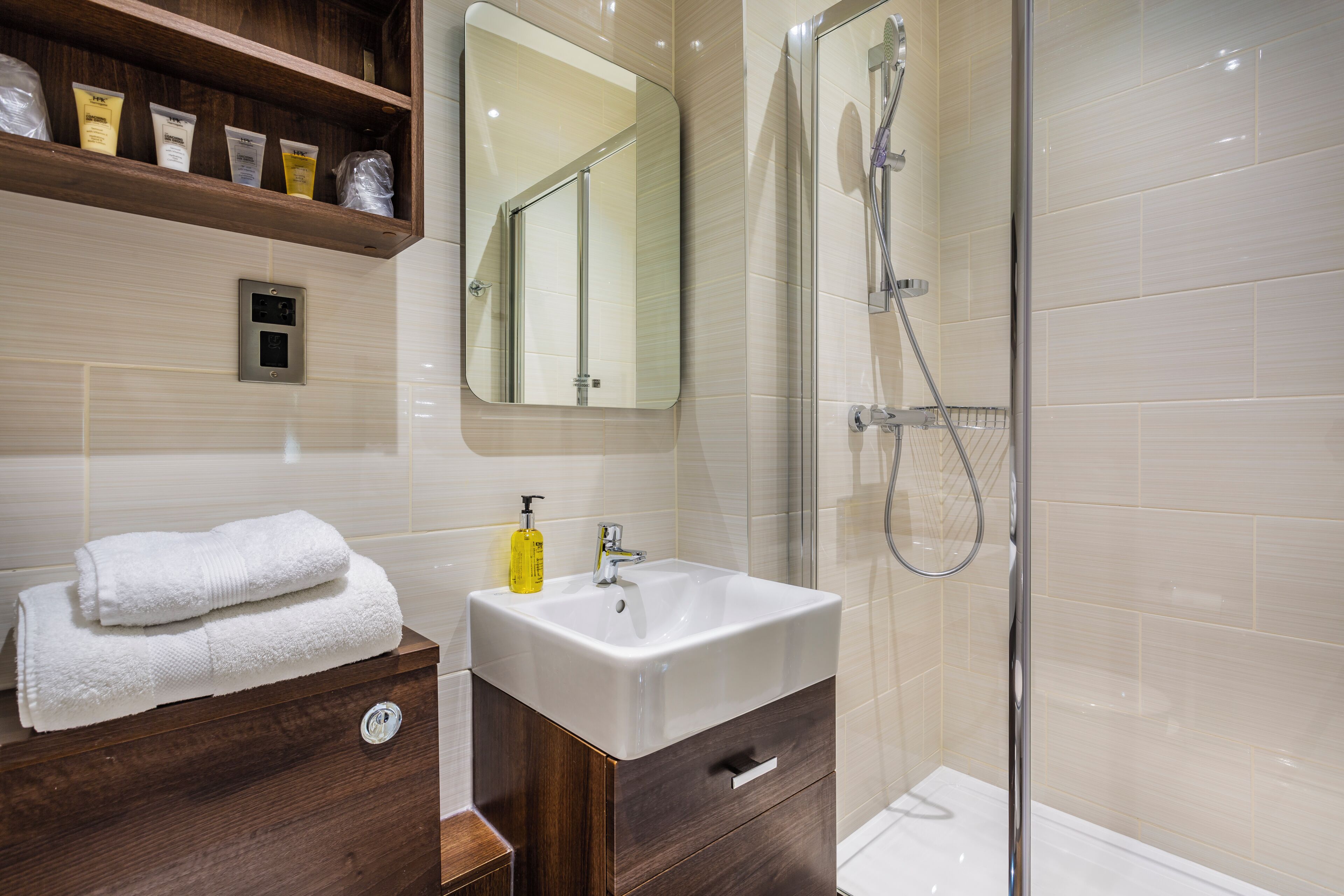 A modern bathroom with a vanity, a mirror, a shower, and toiletries on a shelf.