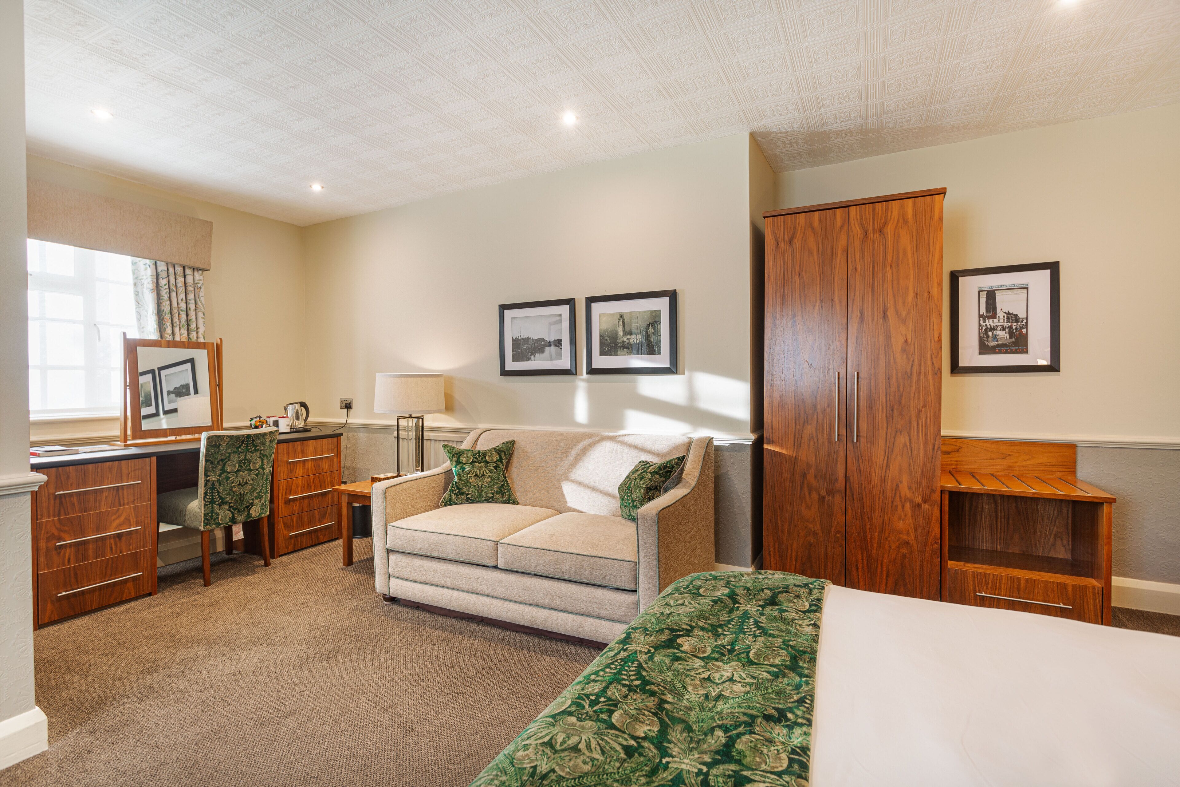 Quarto de hotel com cama, escrivaninha, cadeira, guarda-roupa e duas imagens emolduradas na parede.