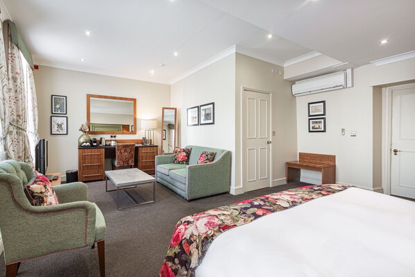 Una habitación de hotel con una cama, un sillón verde, un sofá, un escritorio y un espejo.