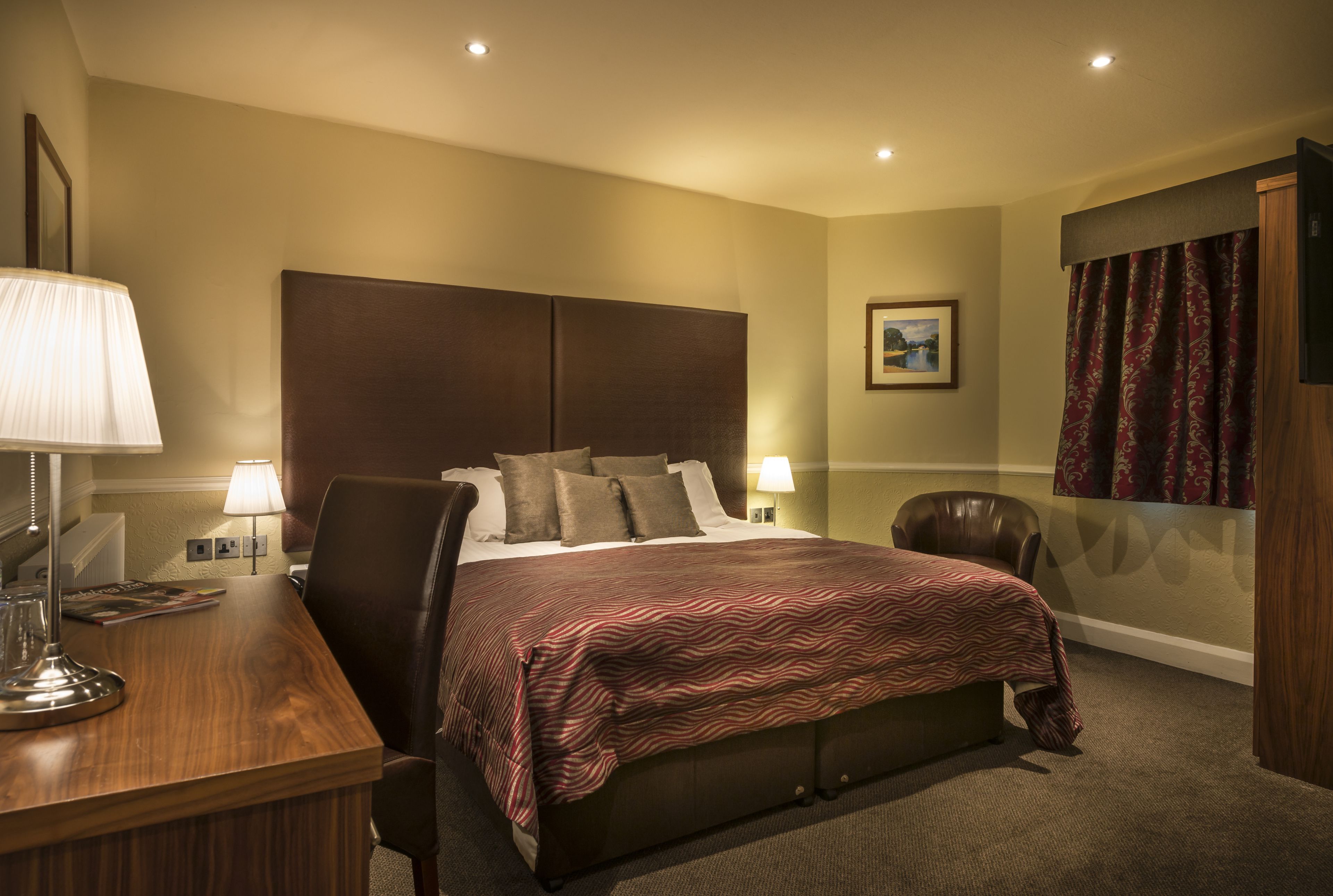 A hotel room with a large bed, a desk with a lamp, a chair, and a picture on the wall.