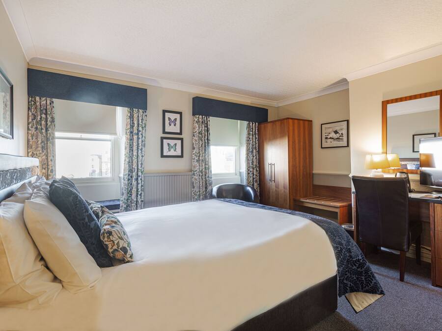 Quarto de hotel com cama, escrivaninha, cadeira e televisão.
