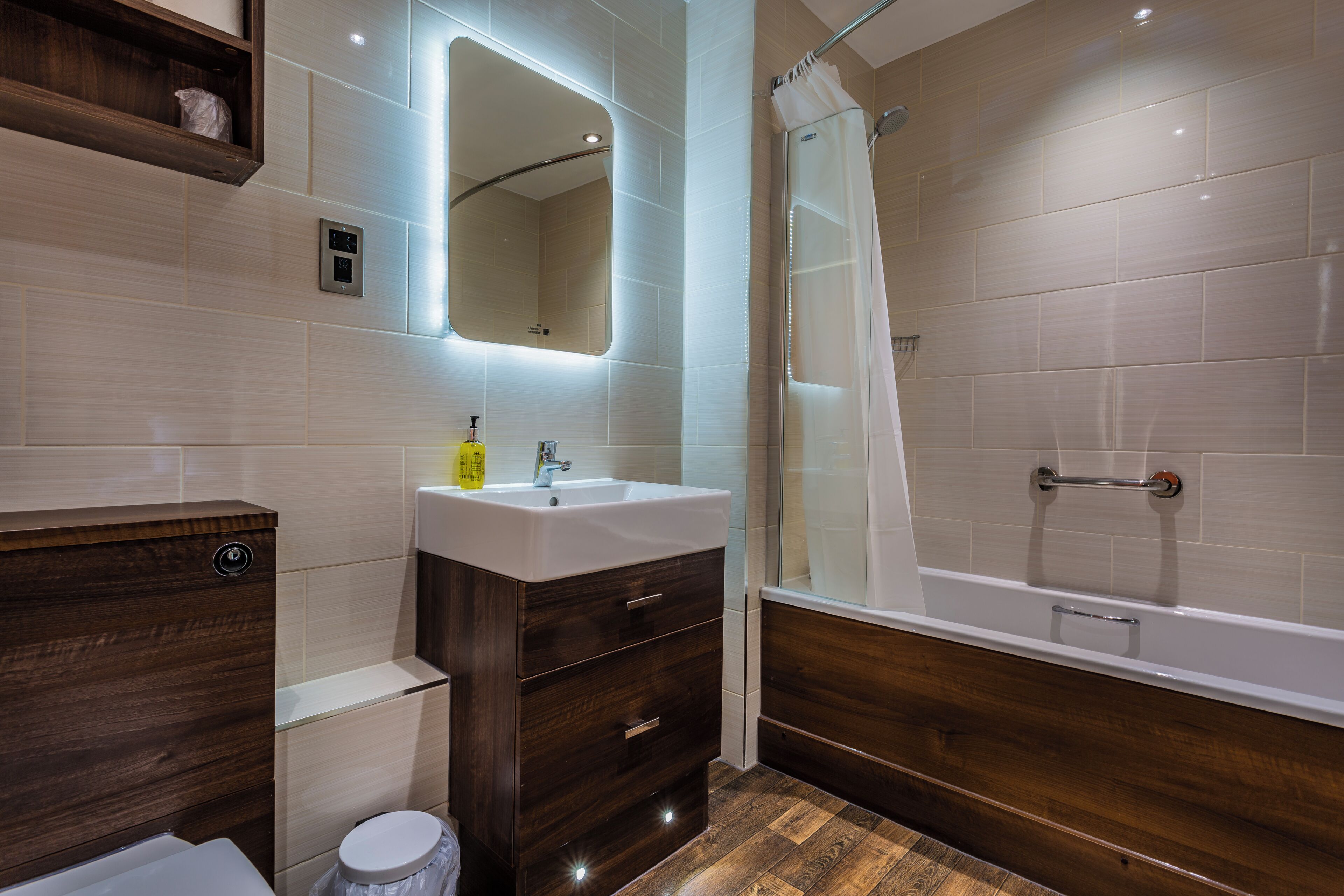 Un baño moderno con un tocador de madera, un lavabo, un espejo y una ducha.