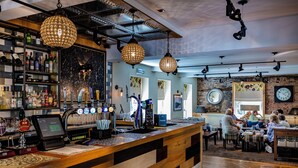 A bar area with a wooden counter, shelves with bottles, and hanging lights.