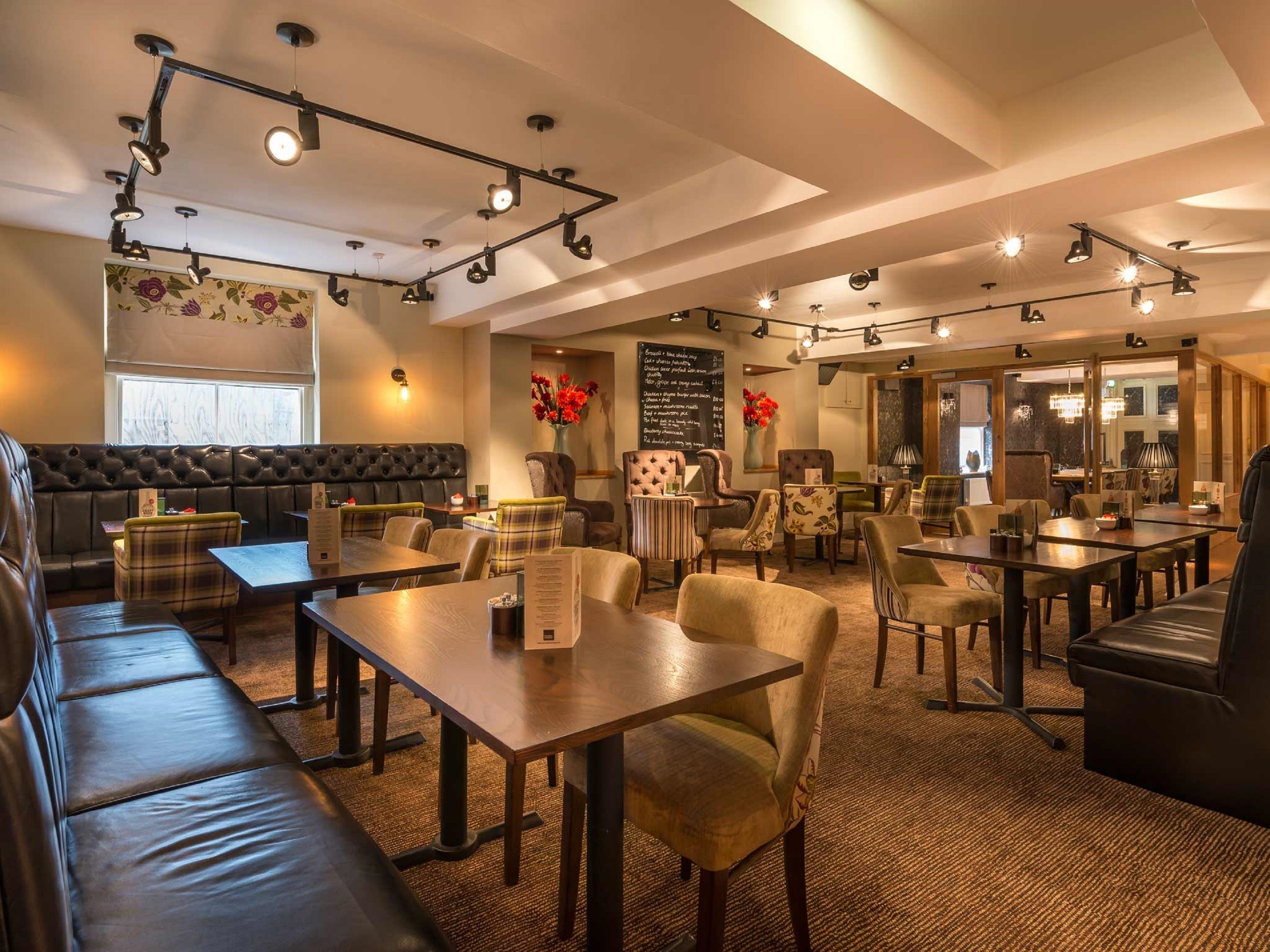 A restaurant with a high ceiling, multiple tables and chairs, a cushioned bench area, and a menu board on the wall.