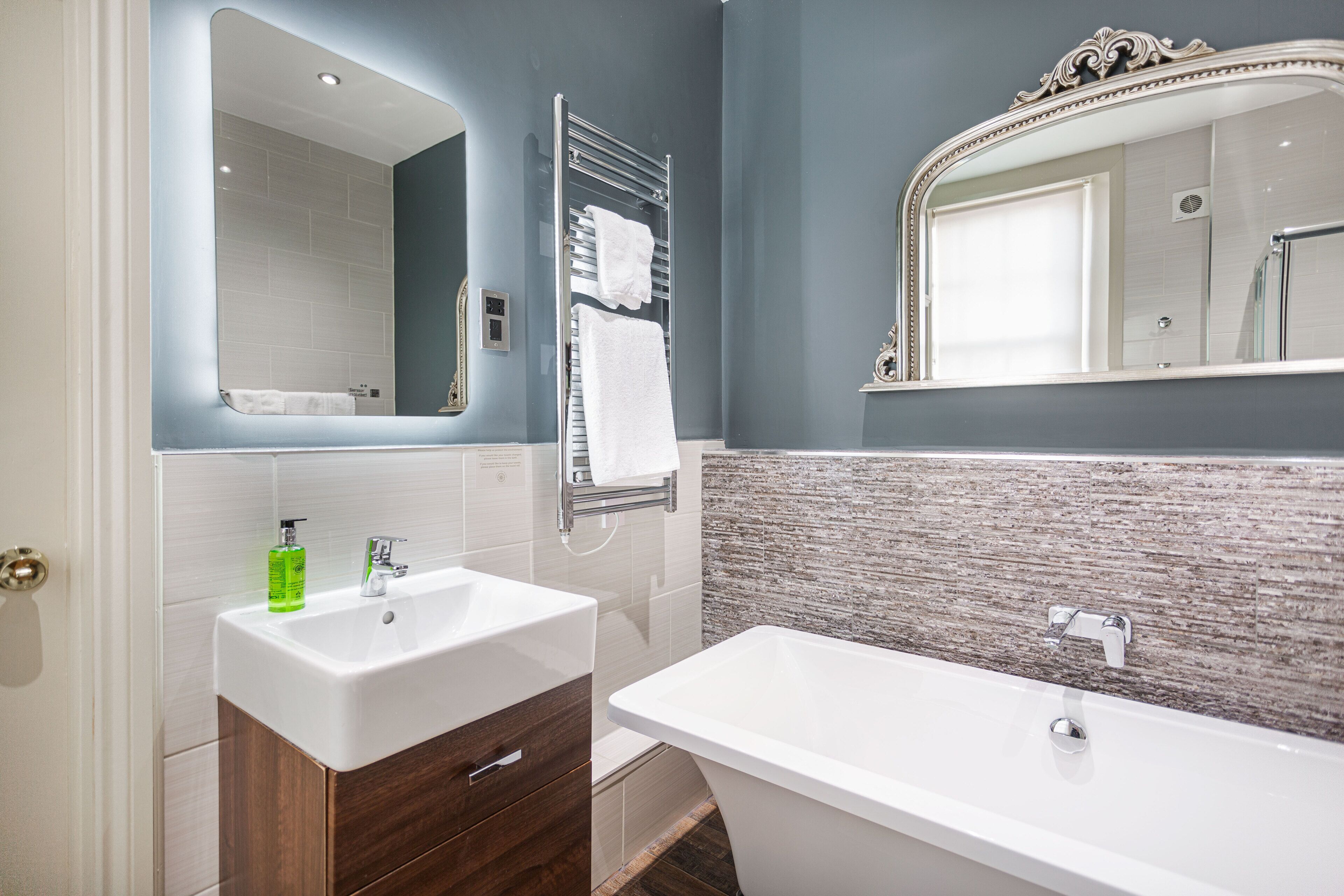 A bathroom with a double sink, a bathtub, a large mirror, and a towel rack.
