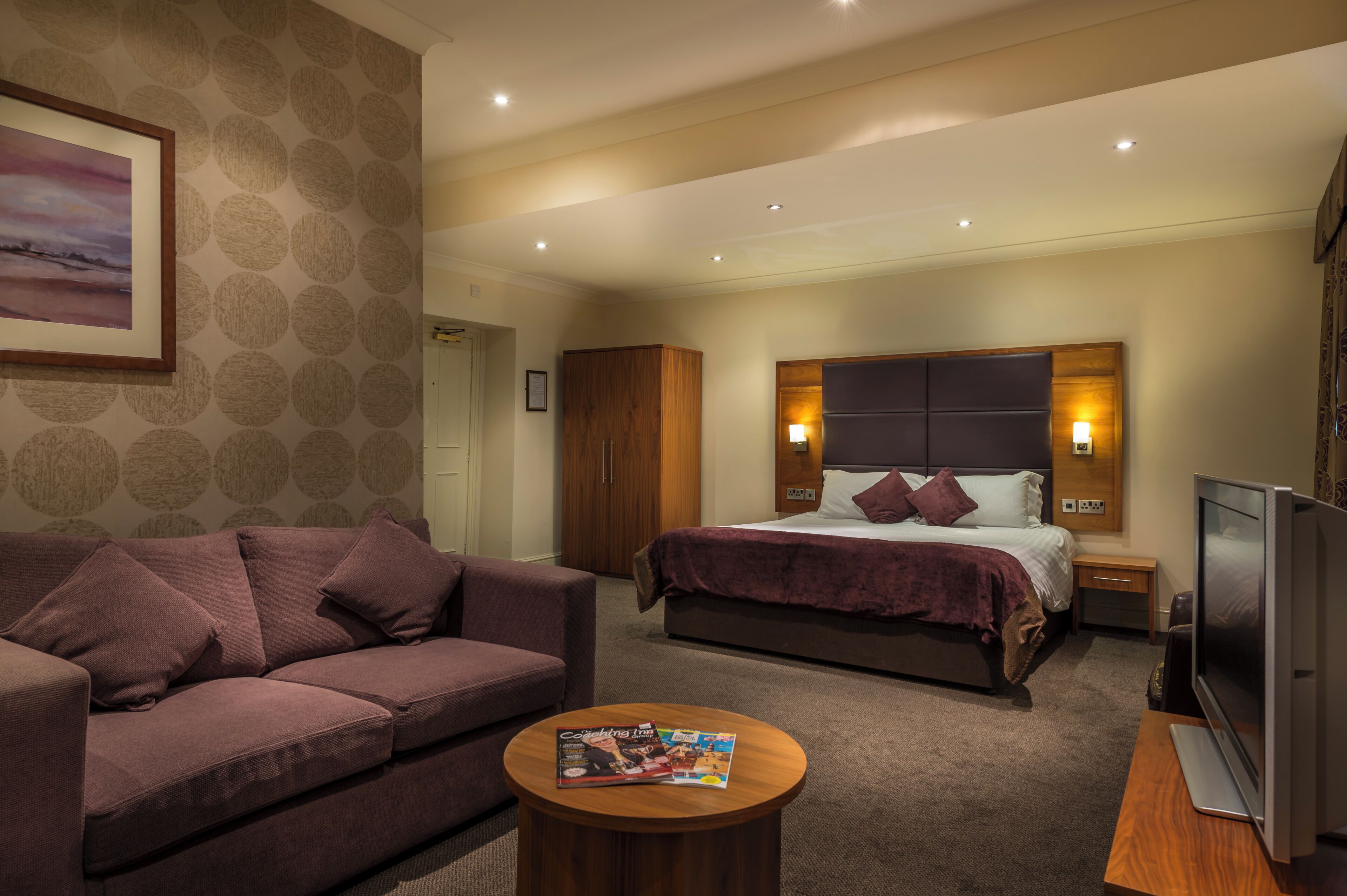 Een hotelkamer met een bed, een bank, een televisie en een tijdschrift op een salontafel.