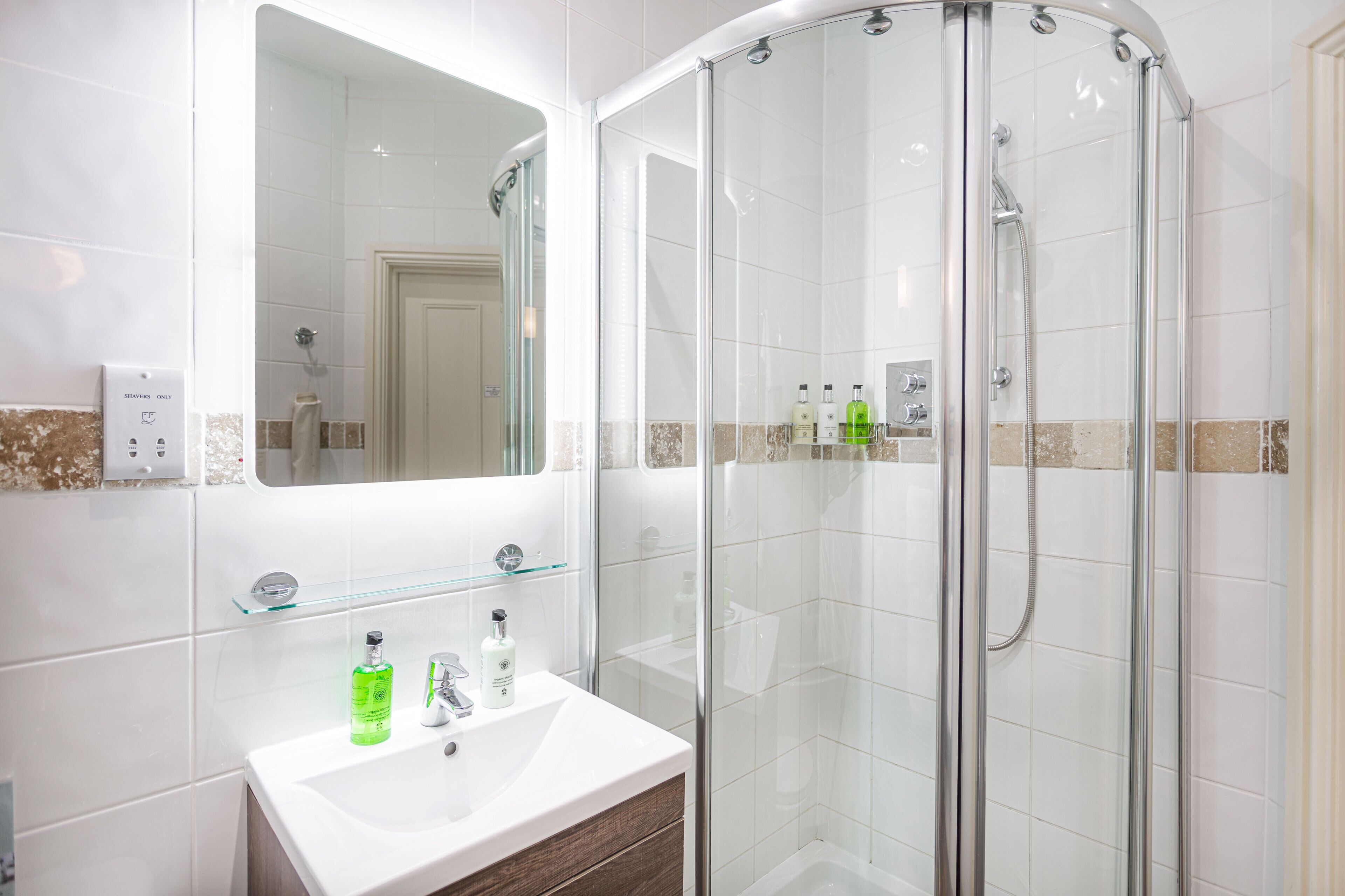 A modern bathroom with a glass-enclosed shower, a white sink with a mirror, and a glass shelf above the sink.