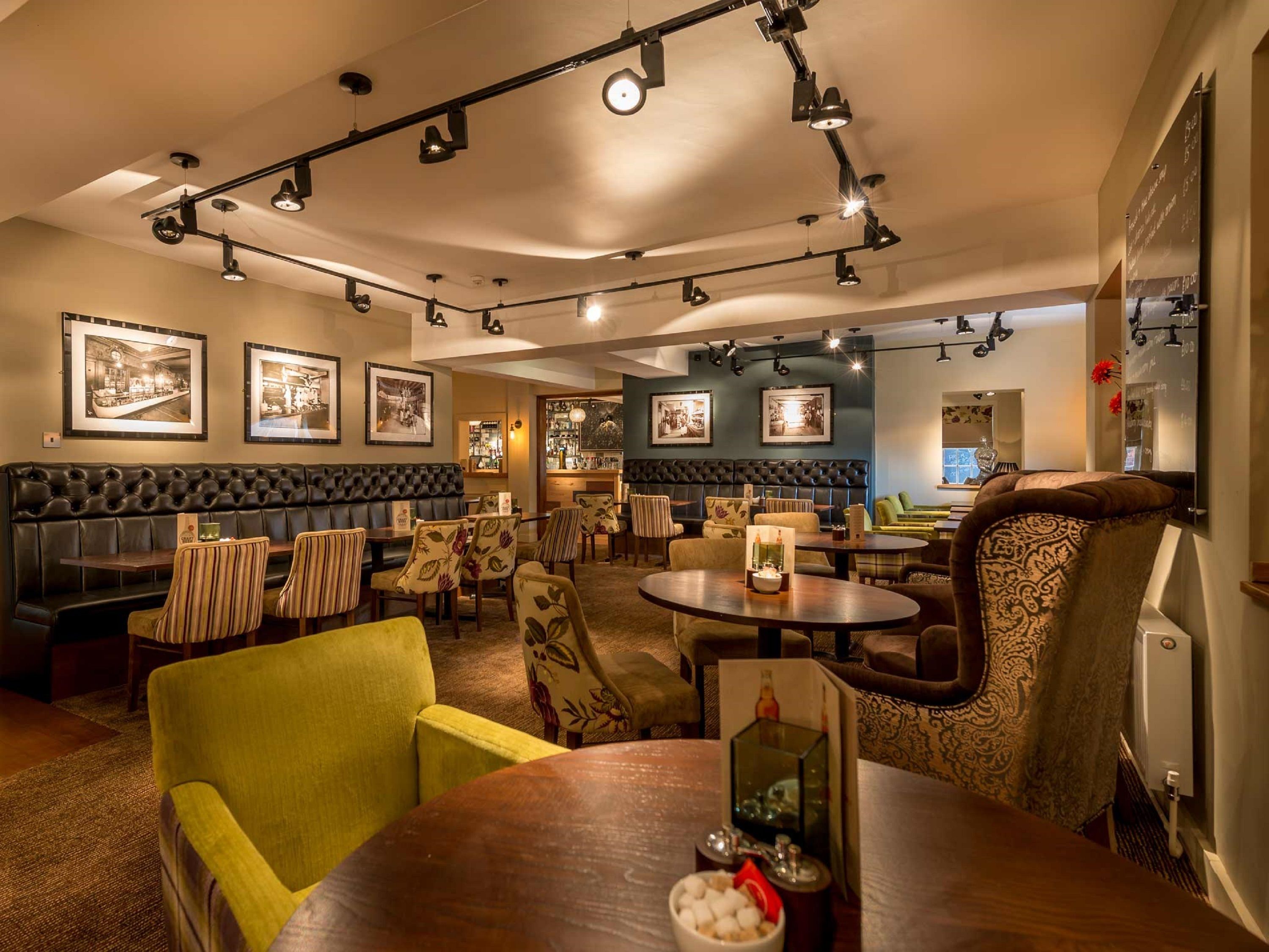 A restaurant with a bar area, leather booths, striped chairs, and tables with a candle centerpiece.