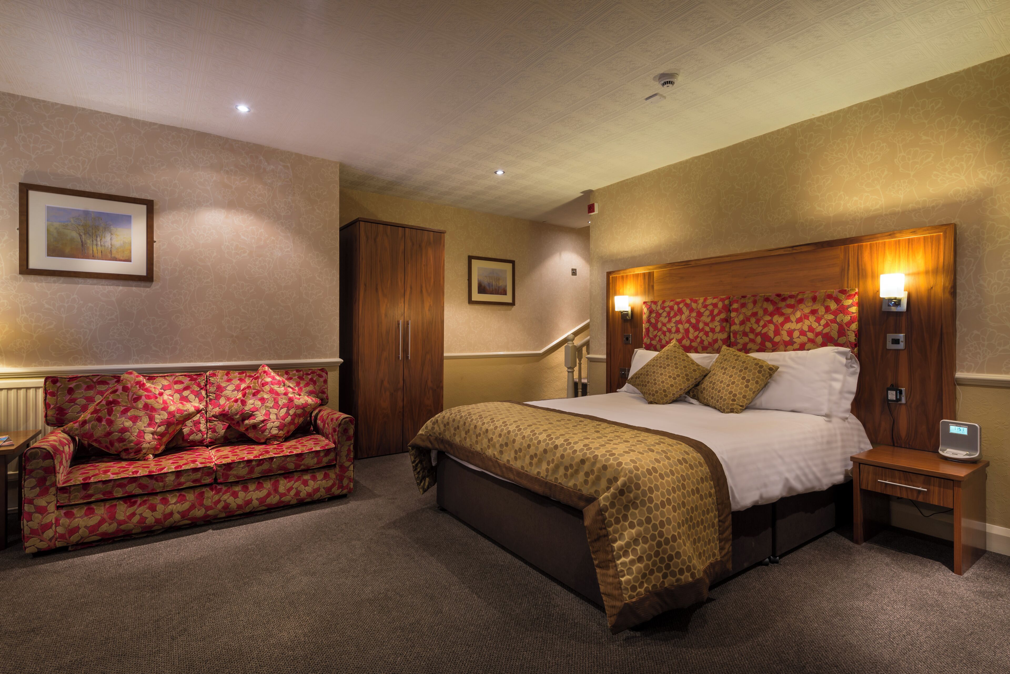 A hotel room with a bed, a sofa, a nightstand, a lamp, and a picture on the wall.
