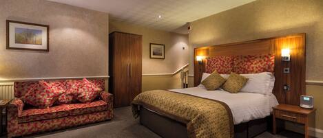 A hotel room with a bed, a sofa, a nightstand, a lamp, and a picture on the wall.