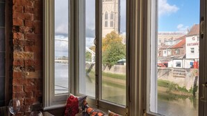 A room with a brick wall, large windows, and a view of a historic building across a river.