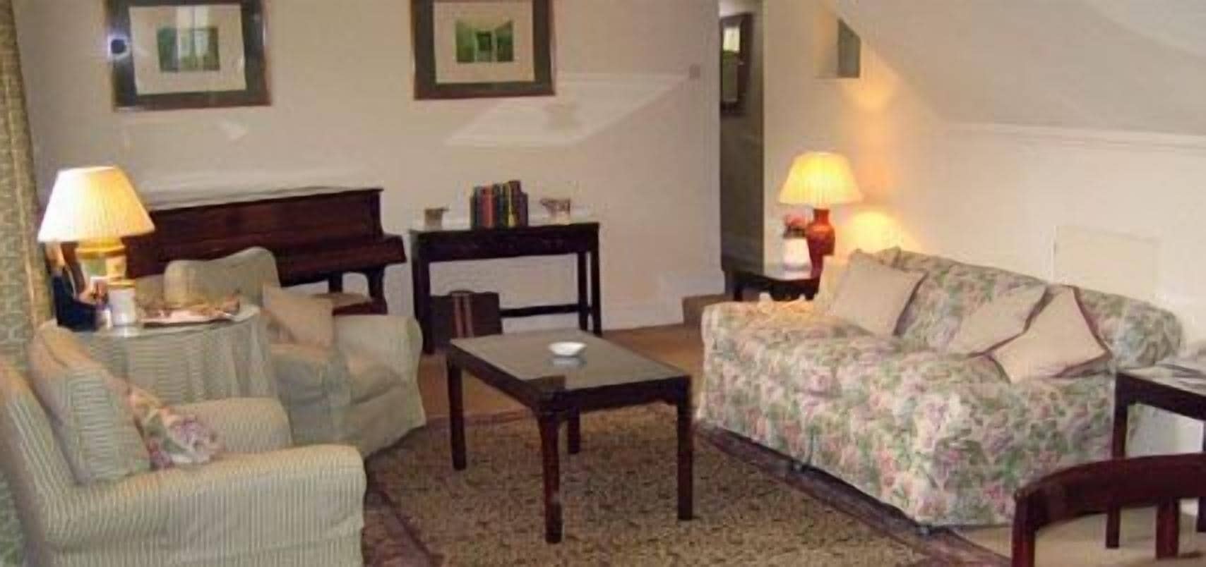 Una sala de estar con sofá, sillones, una mesa de centro y lámparas. En la pared hay cuadros enmarcados.