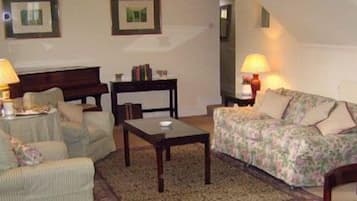 Una sala de estar con sofá, sillones, una mesa de centro y lámparas. En la pared hay cuadros enmarcados.