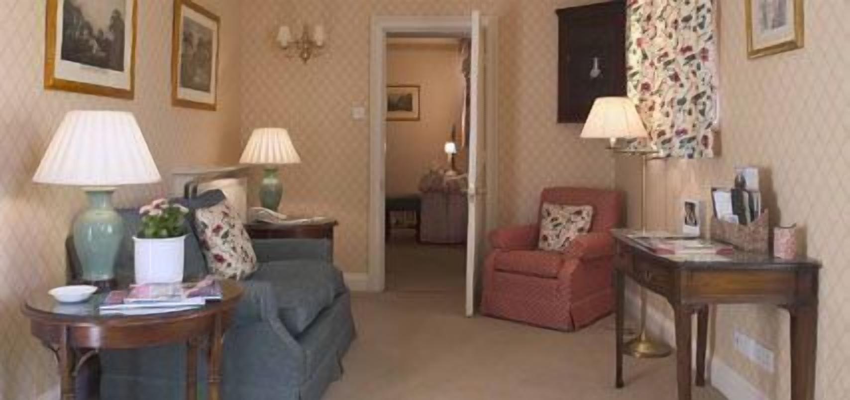 A cozy living room with a sofa, a chair, a table with a lamp, and a small plant.