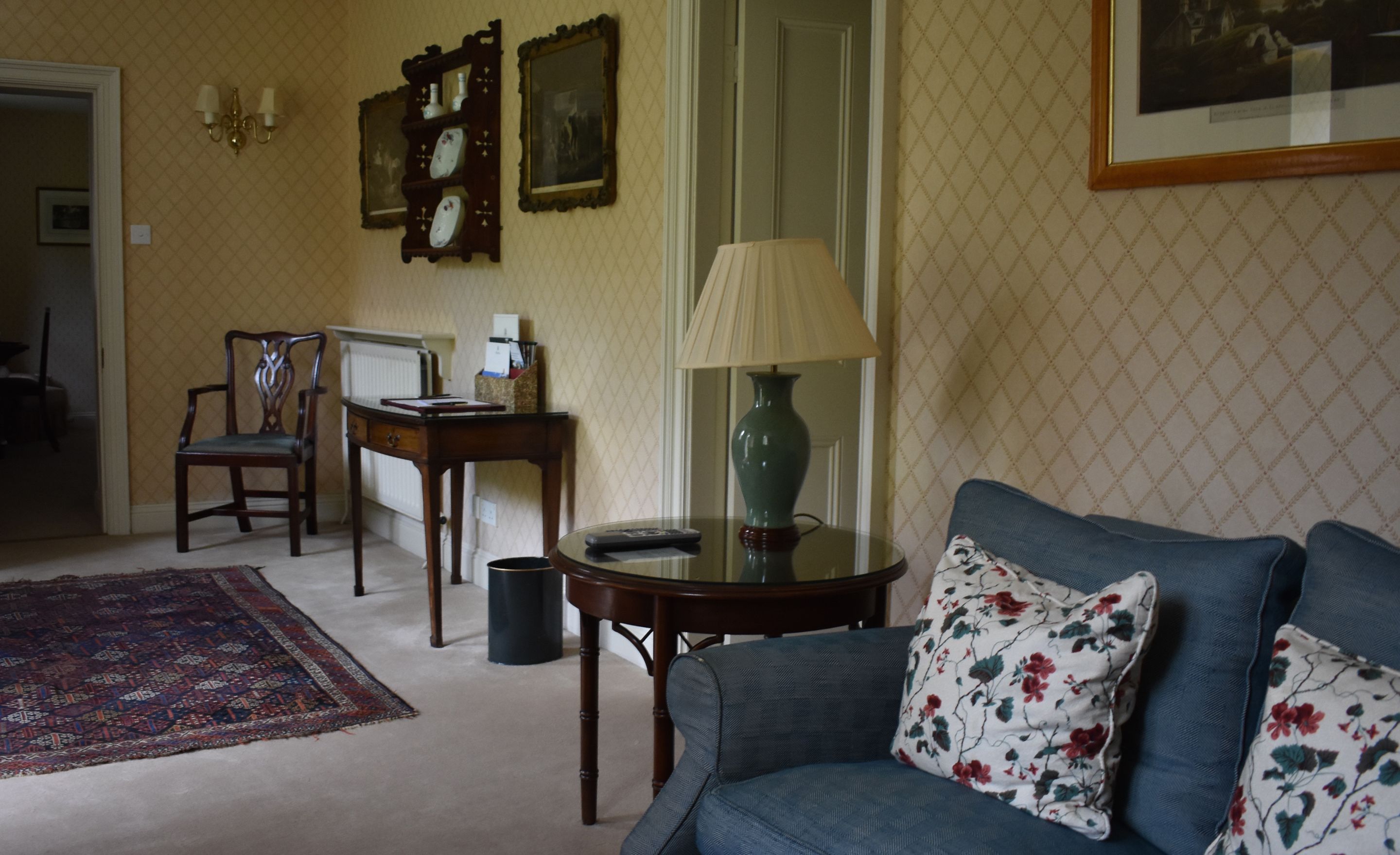 A living room with a sofa, a table with a lamp, a chair, a rug, and wall-mounted decorations.