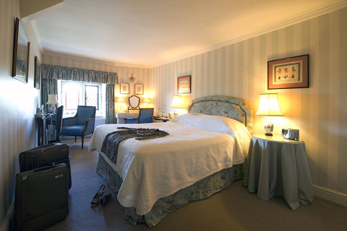 A hotel room with a large bed, a chair, a desk, and a table with a lamp.