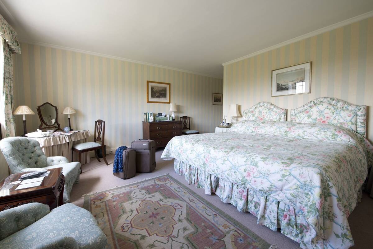 A hotel room with a large bed, a desk with a chair, a dresser, and a small table with lamps.