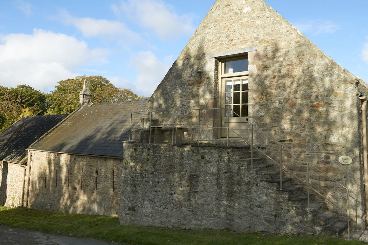 A stone building with a steeply pitched roof, a small window, and a staircase leading up to a door.
