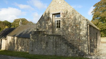 A stone building with a steeply pitched roof, a small window, and a staircase leading up to a door.