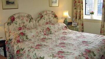 Een slaapkamer met een bloemenbedekking, twee bedlampjes, een nachtkastje en een raam met gordijnen.