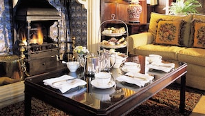 A cozy room with a fireplace, a dining table set for tea, and a comfortable sofa. - Bodysgallen Hall & Spa (Llandudno)