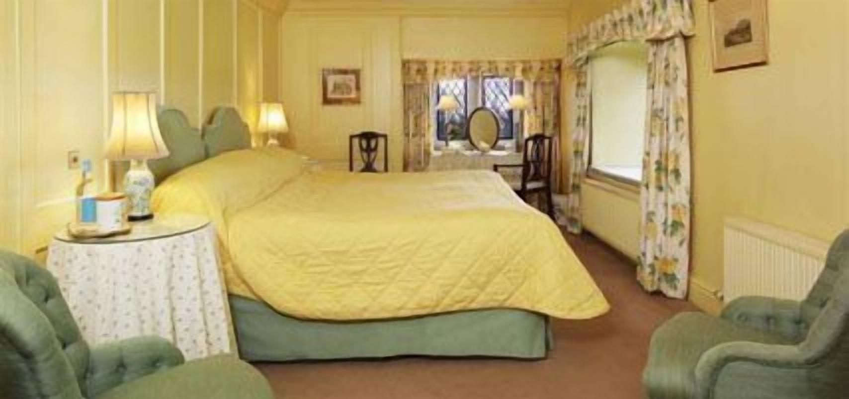 Quarto de hotel com uma cama grande, duas mesas de cabeceira com abajures, uma cadeira e uma janela com cortinas.