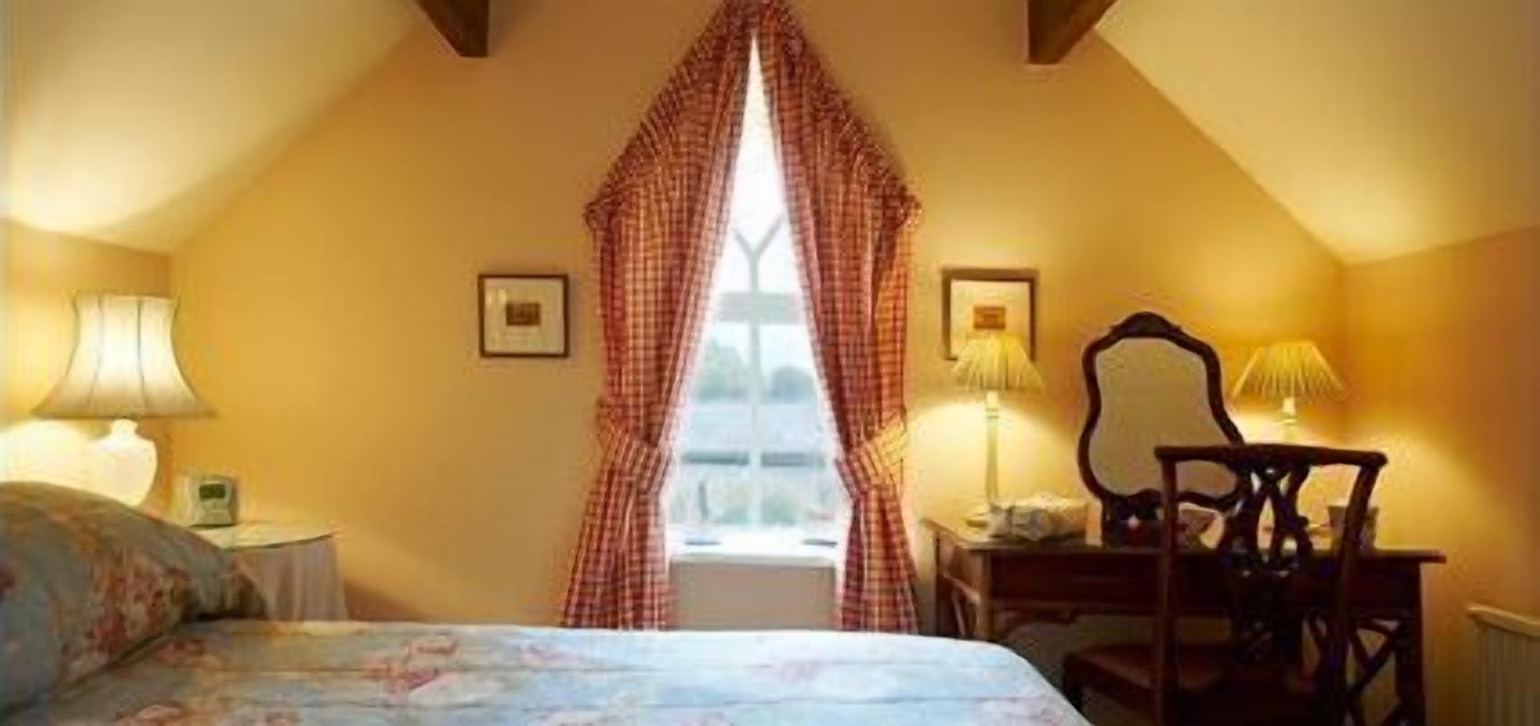 A bedroom with a bed, a chair, a desk, and a window with curtains.