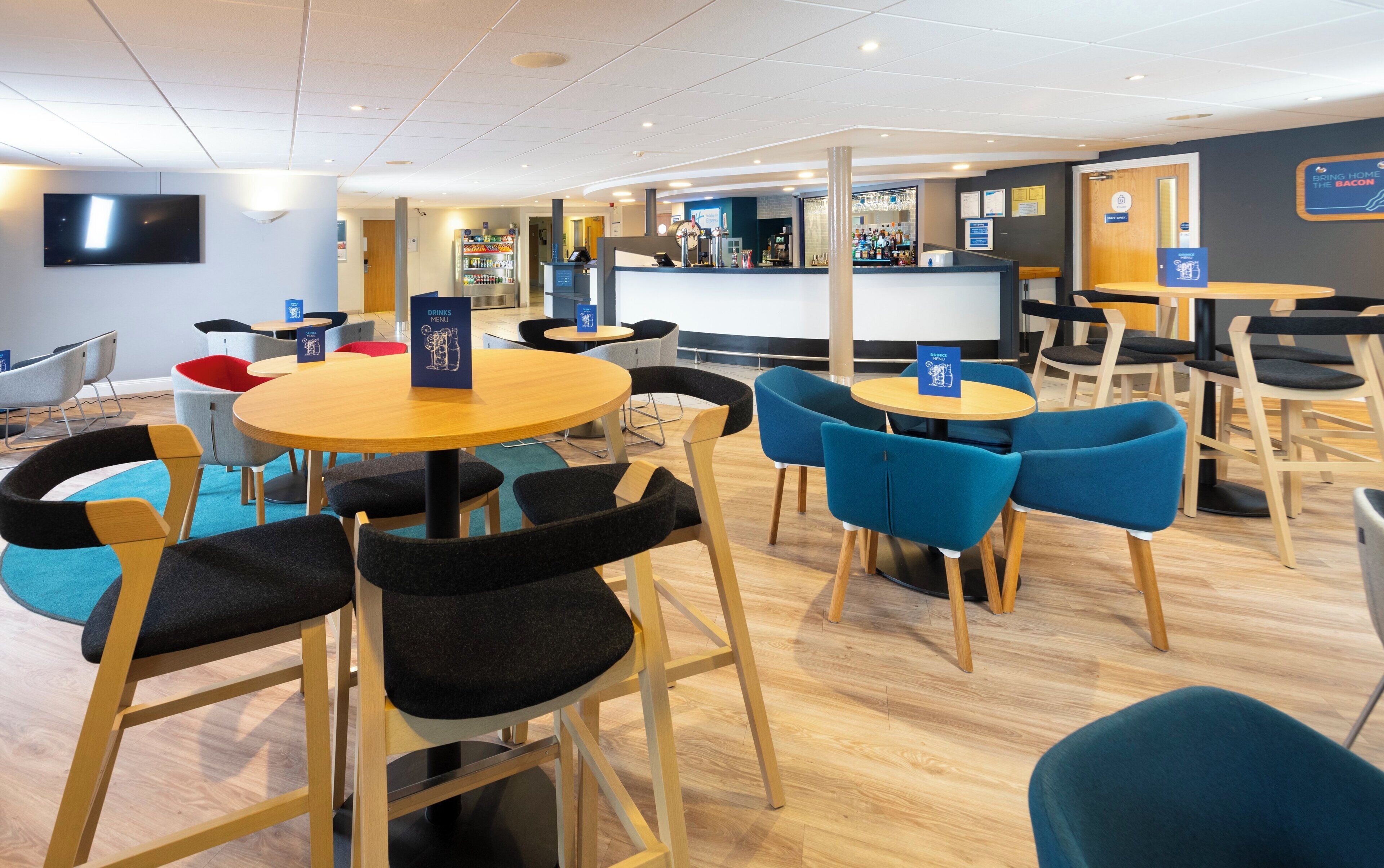 A modern restaurant with round tables and chairs, a bar area, and a television screen.