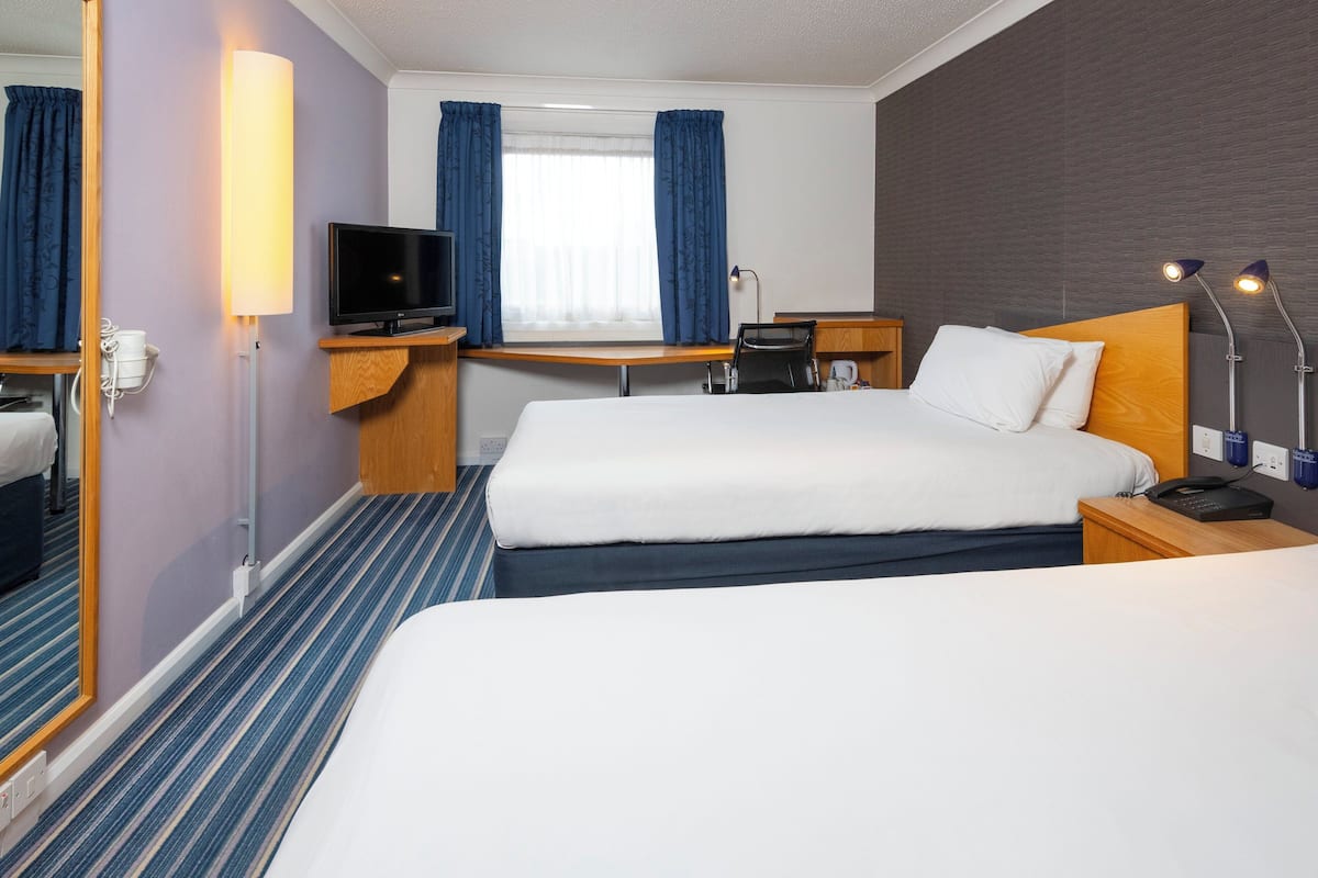 Een hotelkamer met twee bedden, een bureau, een televisie en een raam met gordijnen.