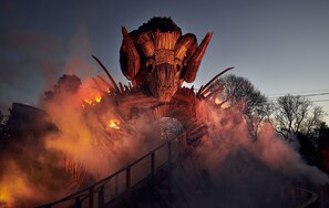 Une grande structure illuminée, dotée d’une tour centrale et de bras qui l’entourent, le tout enveloppé de fumée et de flammes.