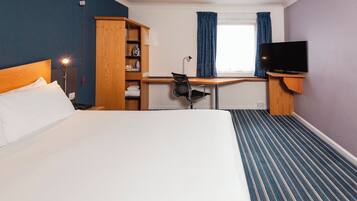 Una habitación de hotel con cama, escritorio, silla, televisor y armario.